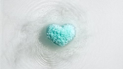 Blue Bath Bomb Ball in the Shape of a Heart Dissolves in Water with White Foam Bubbles Cosmetic