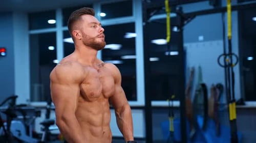Model bodybuilder poses to the camera and shows perfect abs and strong body. Slow motion.