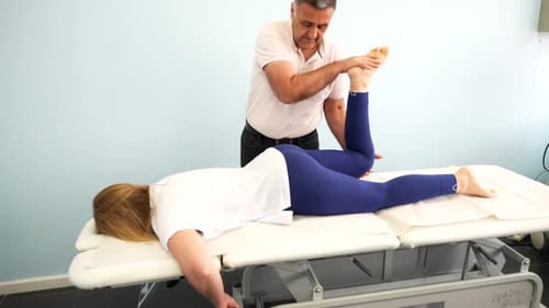 Physiotherapist performs hip flexibility exercises with female patient