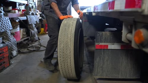 Truck Repair Workshop Mechanic Rolls Removed Tire of the Trailer