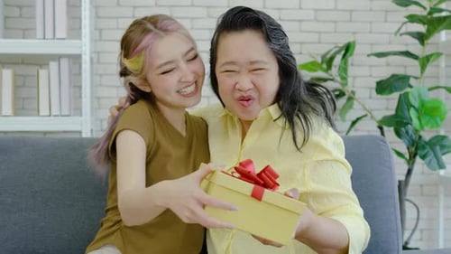 Loving asian teenage daughter giving present to her senior mother. Young woman giving surprise