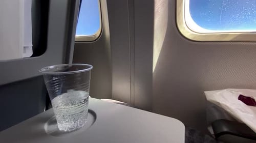 Ein durchsichtiger Plastikbecher mit Wasser mit Gasblasen auf einem Flugzeugtisch