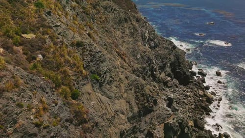 Flight over the cliff on the coastline of Pacific ocean. Some grass and moss covering the shore.