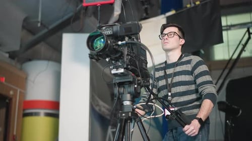 Camera Operator Adjusting Broadcast Camera on Tripod in Tv Studio Preparing for Shooting