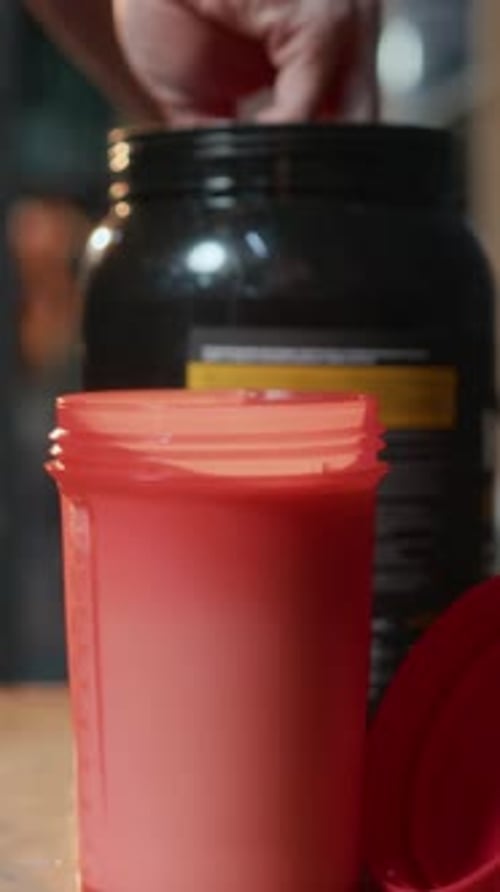 Femme méconnaissable ajoutant une cuillère de poudre protéinée au lait en bouteille