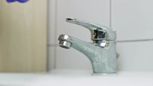 Caucasian hand with purple glove washes faucet to prevent coronavirus