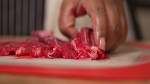 Taking fresh, raw, juicy slices of beef steak and cutting them into cubes - slow motion isolated clo