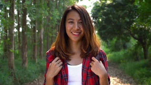 Happy young Asian woman traveler with backpack walking in forest.