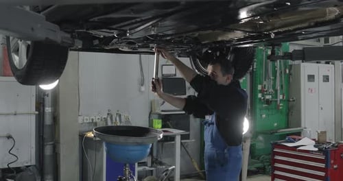 Auto Mechanic Working Under The Car In Dealer's Garage.
