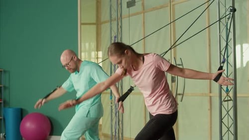 Sportswoman with a Personal Trainer Does Exercise with the Help of Expanders