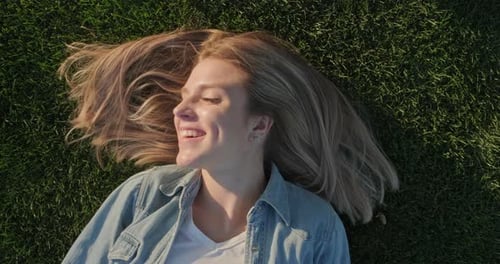 Vista superior del rostro feliz y sonriente de una joven y hermosa mujer acostada en la hierba verde, día cálido y soleado