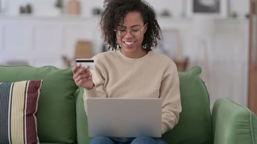 Online Shopping Success on Laptop By Young African Woman on Sofa