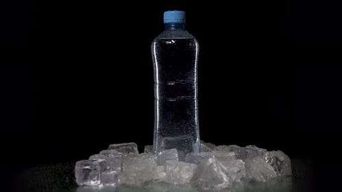 Transparent Bottle with Fresh Pure Mineral Water Spin on Table. Bottle Stands on Black Table