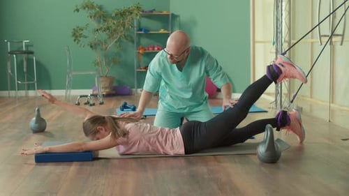 A Physiotherapist Helps a Girl Do Exercises to Relieve Her Back Pain