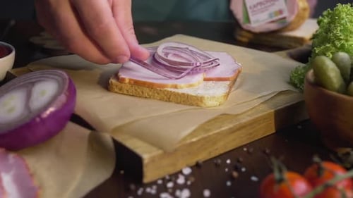 The Cook Adds Sliced Red Onion To the Sandwich with Ham and Vegetables on the Wooden Board in the