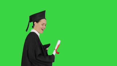 Happy Female Student in Graduation Robe Walking and Cheering with Her Diploma on a Green Screen