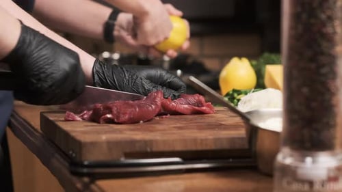 Chef in Restaurant Kitchen Cuts Red Meat or Lamb with Sharp Shiny Knife