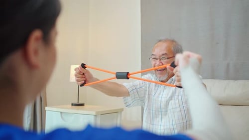 Asian Disabled senior elderly man sitting on sofa doing physiotherapist with support from therapist.