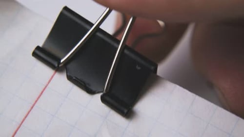 Man Puts Black Clamp on Checkered Paper Sheets Macro