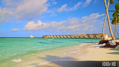 Paradise view of calm island waves along the beach with overwater villas in the distance