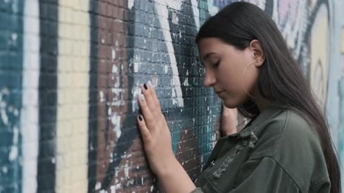Beautiful Hipster Girl Posing Near the Wall with Graffiti. Hands on the Wall