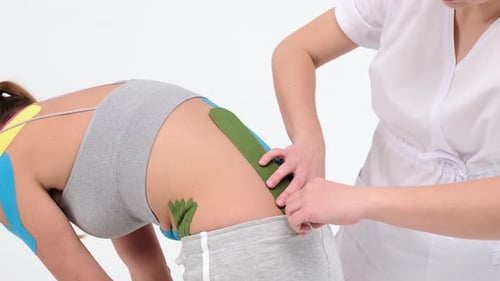 Physiotherapist sticks kinesio tapes to the small of the back of female patient, kinesiology taping