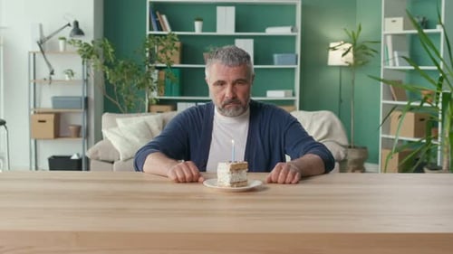 Sad Elderly Man Celebrates the Holiday Alone Looking Thoughtfully at the Cake