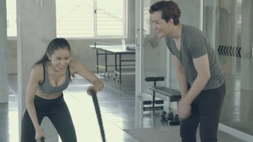 Young asian woman strong doing battle rope exercise in the gym.