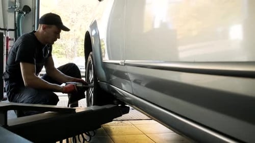 Car mechanic screwing or unscrewing car wheel of lifted automobile at repair service station