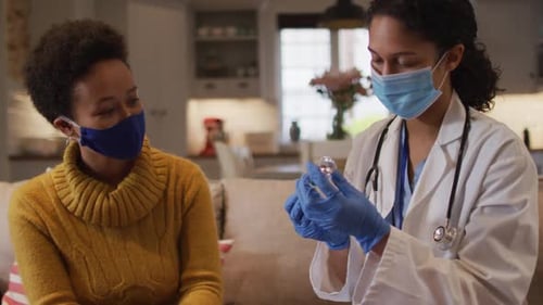 Mixed race female doctor wearing face mask filling syringe at home