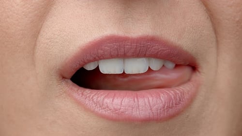 Une femme lèche ses lèvres de près. La langue féminine douce lèche de belles dents blanches