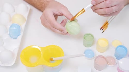 A Man Painting an Egg with Easter Eggs on a White Background Top View