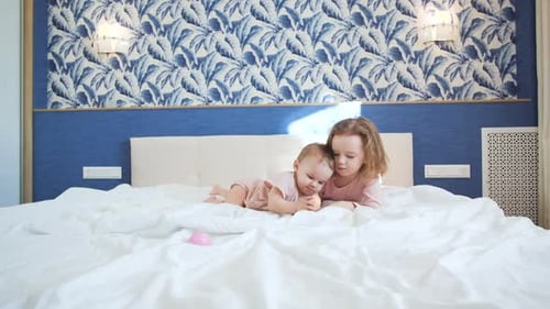 Two Sisters Play Early in the Morning in Bedroom on White King Size Bed