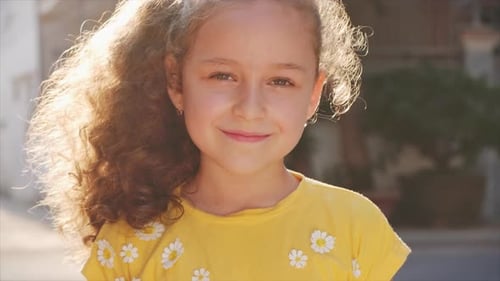 Funny Little Girl Smiles, Looking at the Camera on the Street, a Cute Child Plays on the Street