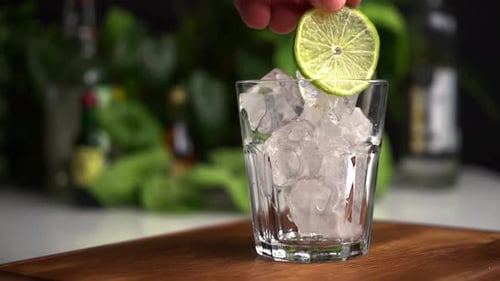 Man Hand Put Lime in Glass of Ice Cubes.
