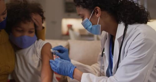 Mixed race female doctor wearing face mask making injection at home