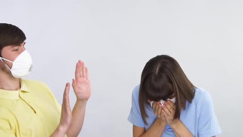 Mujer joven estornudando en un pañuelo de papel y hombre en protección distanciándose de ella