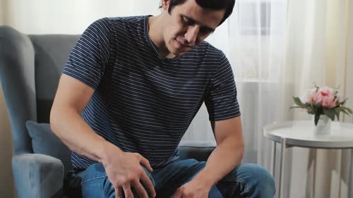 Um homem com dor no joelho sentado na poltrona