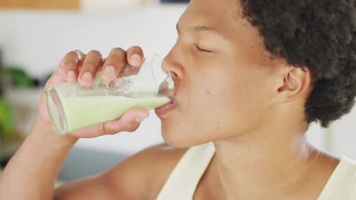 Fit african american man cooking, drinking healthy green smoothie