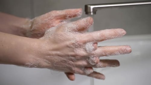A Woman Washes Her Hands with Soap Over a White Sink To Eliminate Germs and Protect Against the