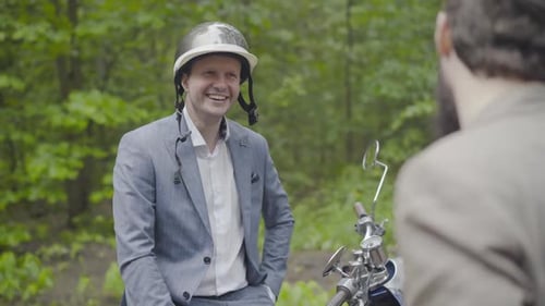 Laughing Adult Man in Bike Helmet Chatting with Bearded Friend Outdoors. Portrait of Happy Positive