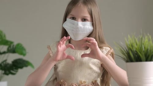 Little Caucasian Girl in Medical Mask Congratulates on Valentine's Day Showing Heart Symbol