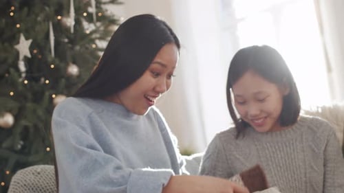 Mulher asiática abrindo presente de Natal e abraçando a família com carinho