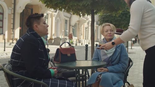 Waitress Bringing Hot Beverages to Charming Middleaged Women Outdoors