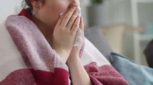 Mujer enferma sentada en el sofá y tosiendo en una servilleta