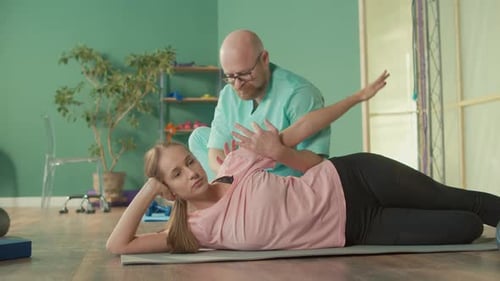 Physiotherapist Helps Girl to Do Exercises to Relieve Pain in Rehab Clinic