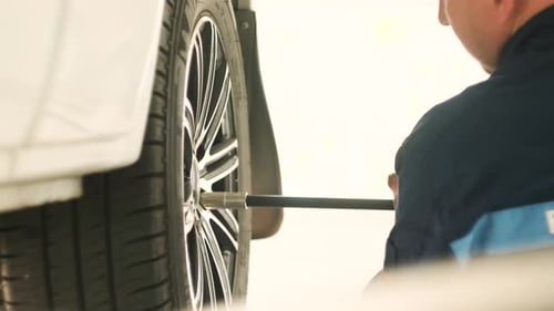 Car mechanic screwing or unscrewing car wheel of lifted automobile at repair service station