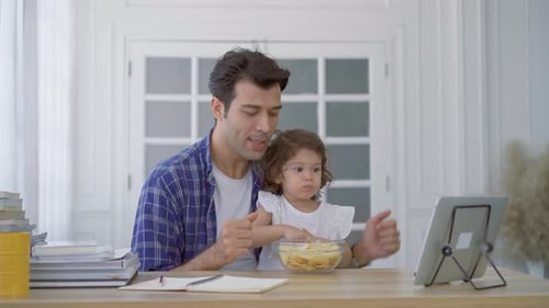 Father and little cute daughter watching the movie or cartoon on the tablet and eating potato chips