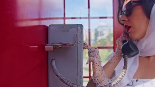 Beautiful Young Woman Happily Speaks on the Phone in an English Style Red Telephone Booth