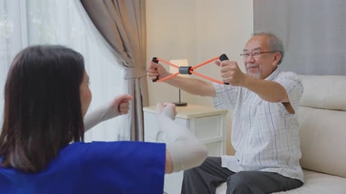 Asian senior elderly man sitting on sofa doing physiotherapist with support from therapist nurse.